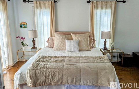 A bed with a beige comforter and pillows is in the center of a room with two lamps on side tables.
