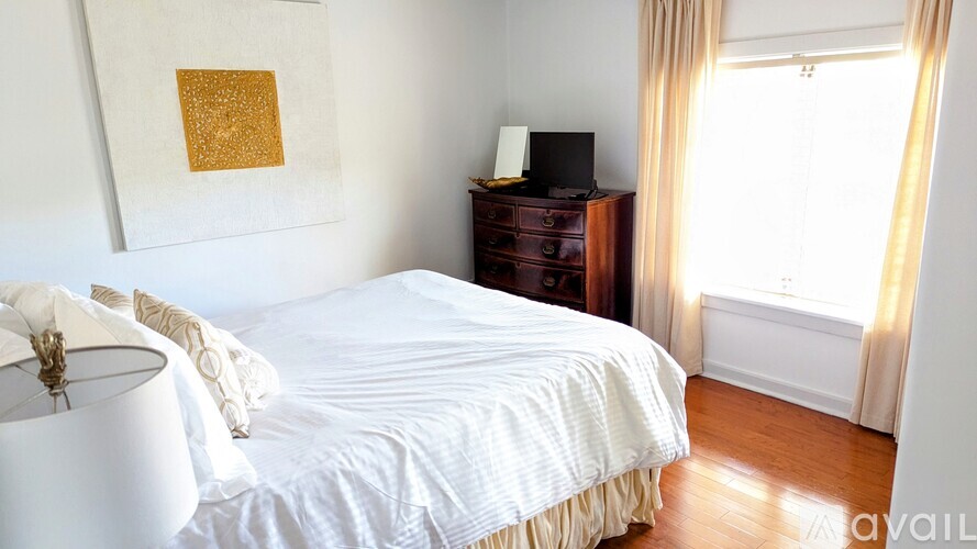 A bedroom with a white bed and a wooden dresser.