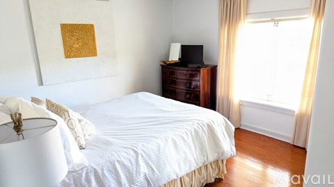 A bedroom with a white bed and a wooden dresser.