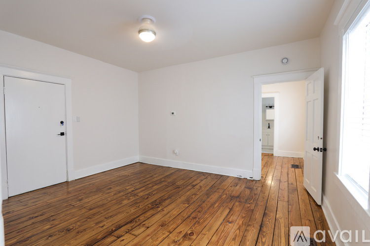 A room with wooden floors and white walls, with a door on the left and a window on the right.