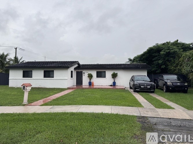 A white house with a red roof and a black car parked in front.