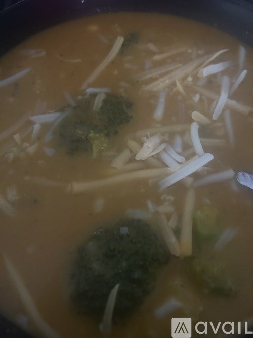 A bowl of soup with broccoli and shredded cheese on top.