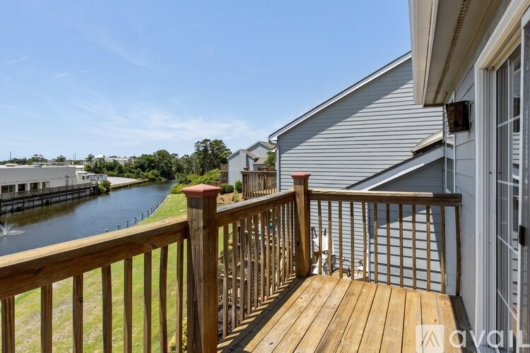 A wooden deck overlooks a body of water with a house in the background.