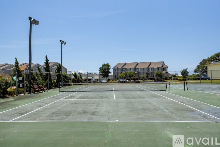 A tennis court with a green surface and white lines, surrounded by trees and buildings.