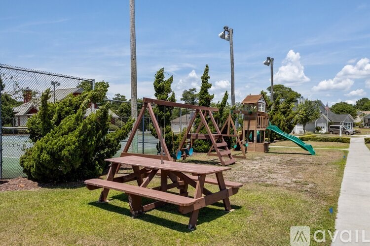 A wooden picnic table is in the foreground of a playground with a green slide.