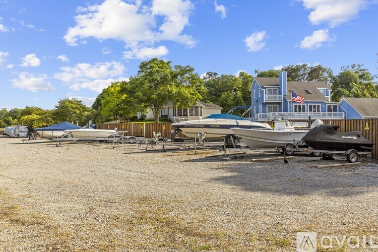 A gravel lot with boats and jet skis in front of a house.