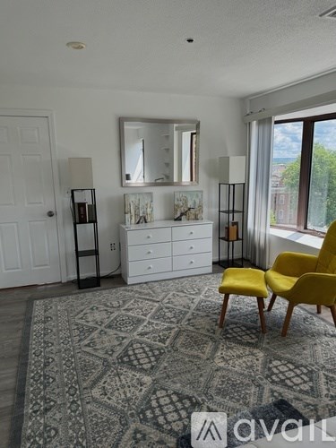 A room with a rug, a yellow chair, a white dresser, and a mirror.