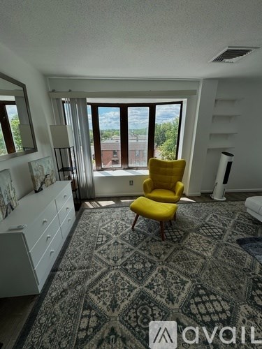 A yellow chair is in the middle of a patterned carpet in a room with a large window.