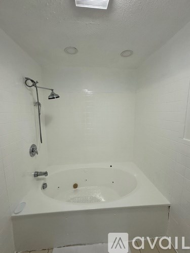 A white bathroom with a jetted tub and a shower head.
