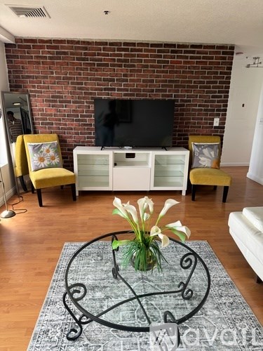 A living room with a television, yellow chairs, and a flower vase on a rug.