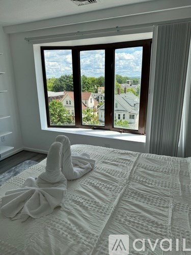 A bedroom with a large bed and a window overlooking a residential area.