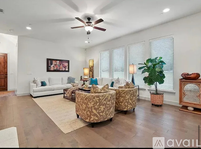 A living room with a white couch, two chairs, and a ceiling fan.