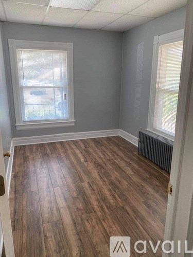 A room with wooden flooring and two windows.
