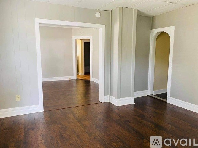 A room with wooden floors and white walls, with a doorway leading to another room.