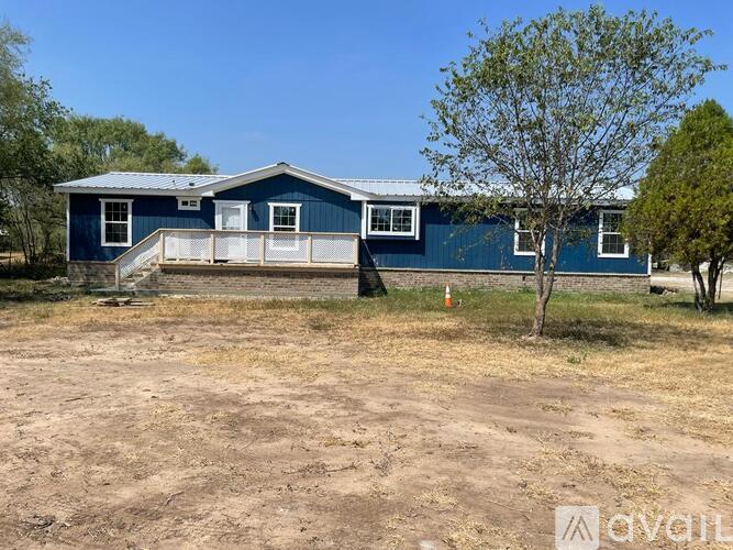 A blue house with a white porch and a tree in front.