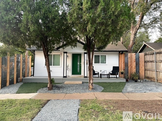 A house with a green door and a white exterior is surrounded by a wooden fence and has a small garden area.