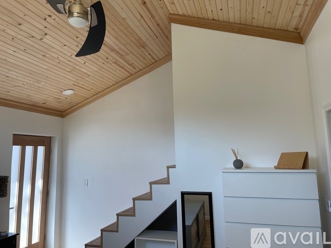A wooden ceiling fan hangs over a staircase in a white room.