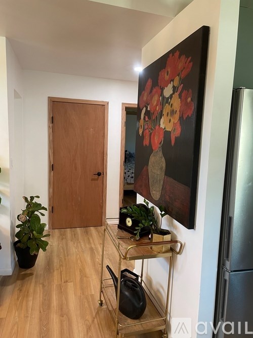A painting of flowers hangs on the wall above a shelf with plants and a bag on it.