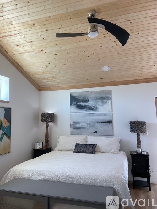 A bedroom with a bed, two lamps, and a painting on the wall.