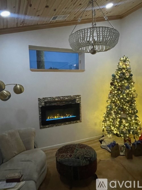 A Christmas tree stands next to a lit fireplace in a cozy room.