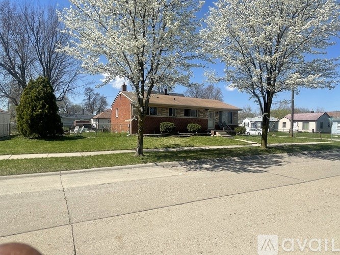 A tree with white blossoms stands in front of a brick house.