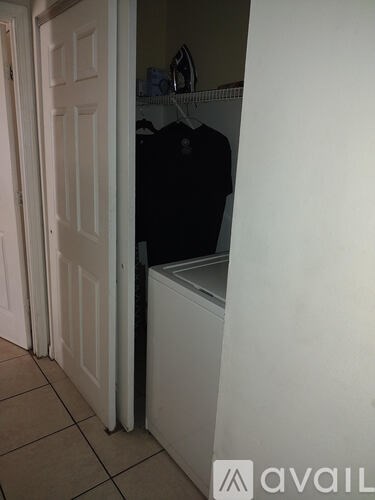 A white door is open to a small closet with a black coat hanging on a rod.
