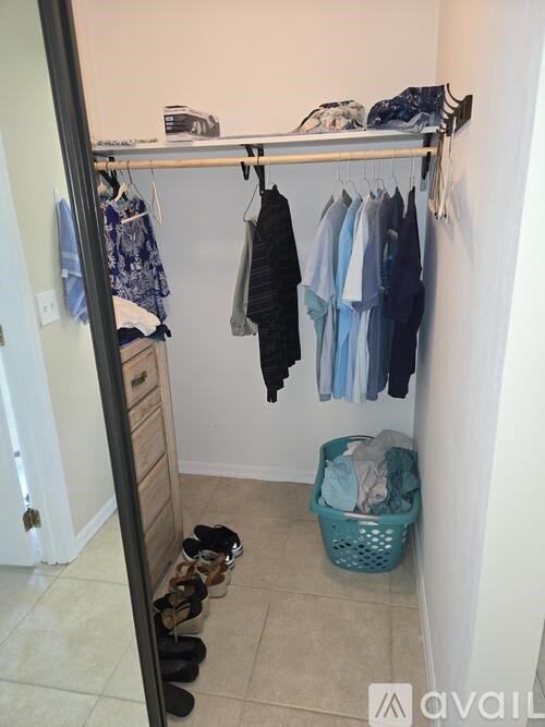 A small closet with clothes hanging and shoes on the floor.