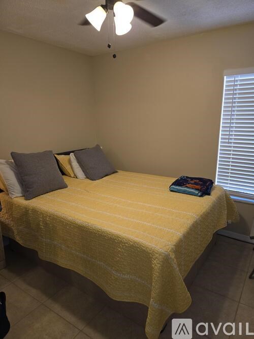 A bed with a yellow cover and two grey pillows in a room with a ceiling fan.
