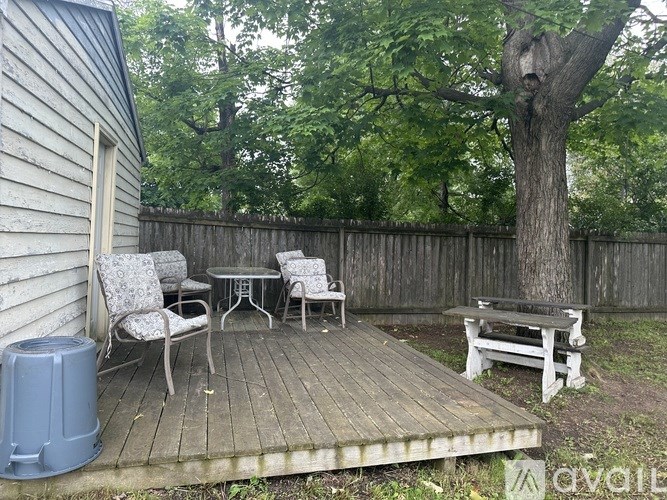 A backyard with a wooden deck, a tree, and a bench.