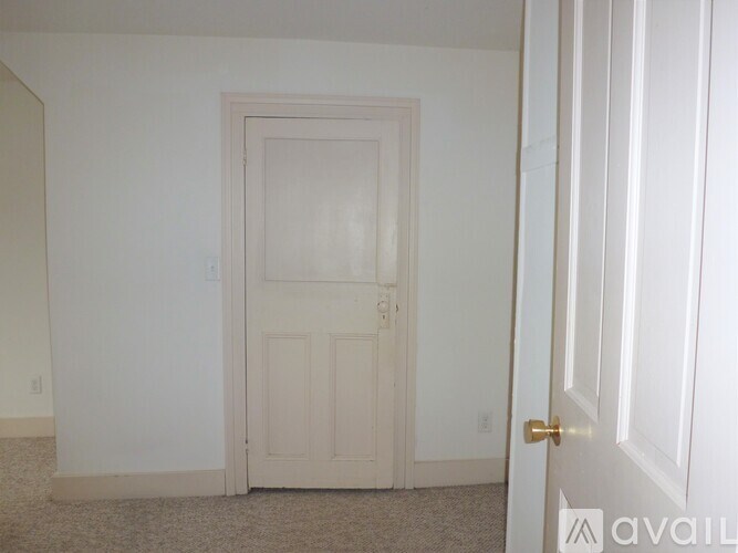 A white door with a gold handle is in a room with a carpeted floor.