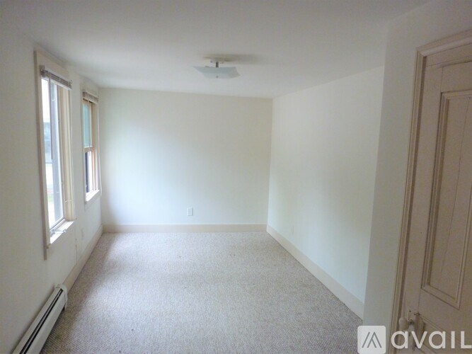 A room with a carpeted floor, a ceiling fan, and a door.