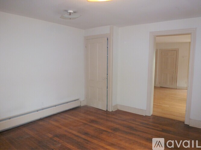 A room with wooden floors and white walls, with a door on the left and another door on the right.