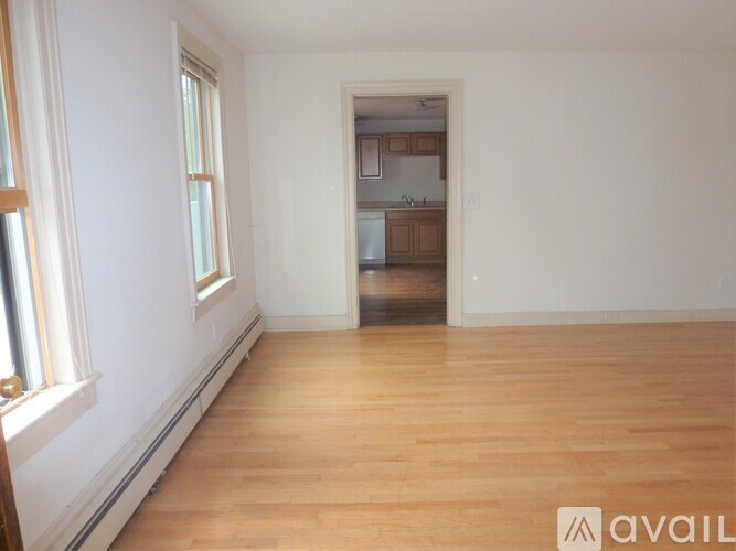 A room with wooden floors and a kitchen visible through the door.