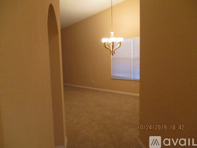 A chandelier hangs from the ceiling in a room with beige walls and carpeting.