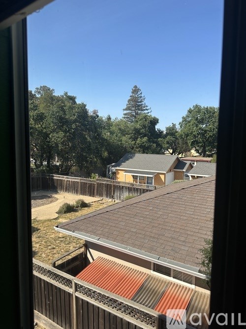 A view from a window looking out to a house with a brown roof and a fence.