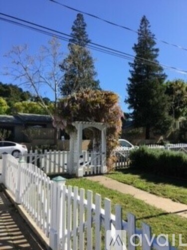 A white picket fence in front of a house with a tree and a car in the background.