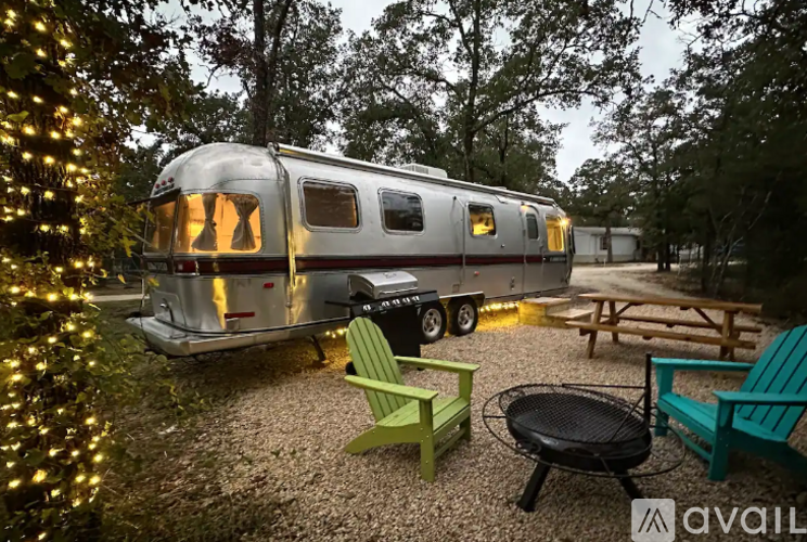 A silver RV is parked in a gravel lot next to a picnic table and chairs.