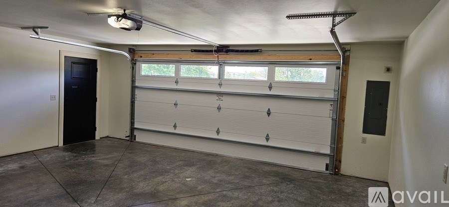A large garage with a white roller shutter door and a black door on the left side.