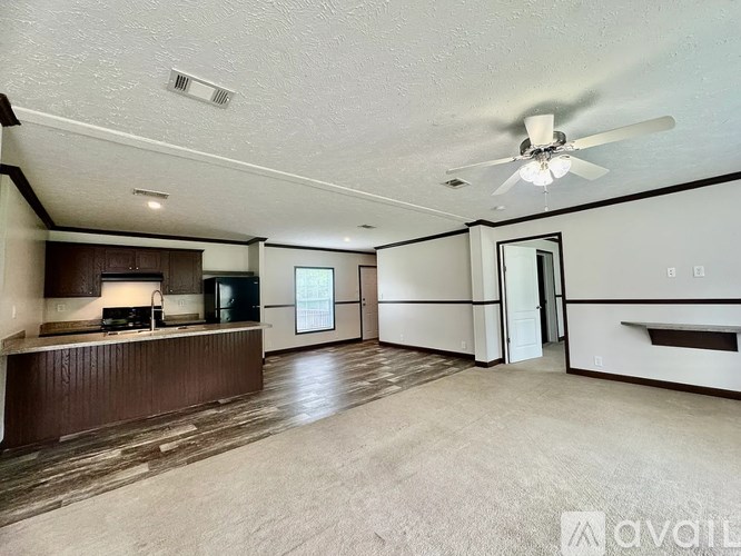 A spacious living room with a ceiling fan and a kitchen area in the background.