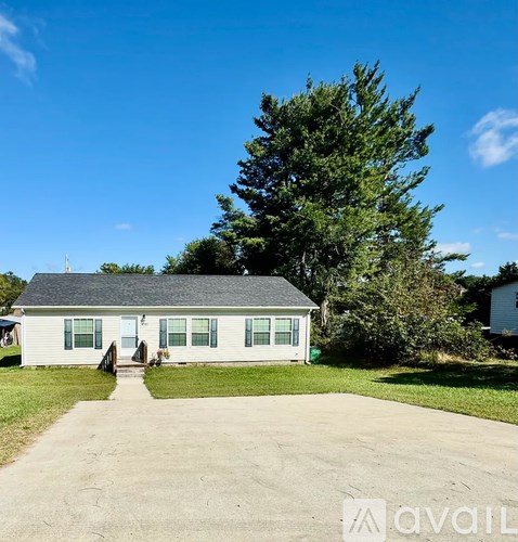 A small white house with a grey roof and a green lawn in front.