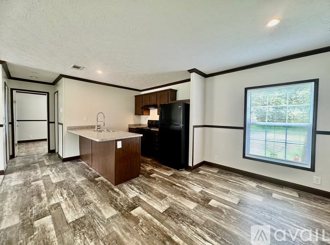 A kitchen with a black refrigerator and wooden flooring.