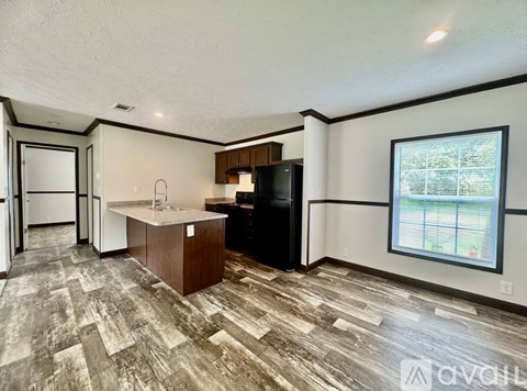 A kitchen with a black refrigerator and wooden flooring.