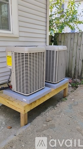 Two air conditioning units are placed on a wooden platform outside a house.
