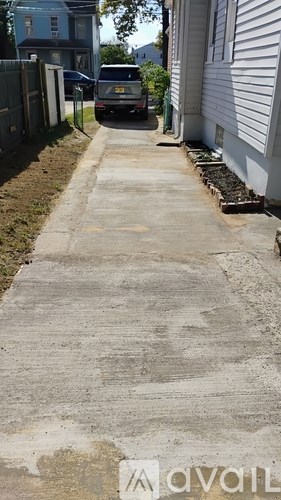 A concrete pathway leads to a house with a car parked on the street.