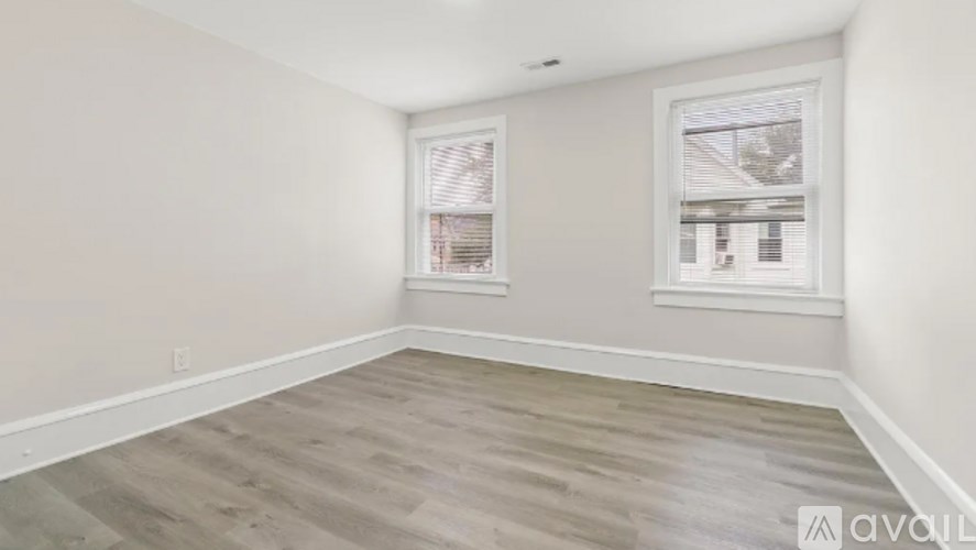 A room with wooden flooring and two windows.