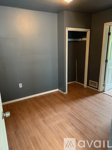 A room with wooden flooring and a door on the left.