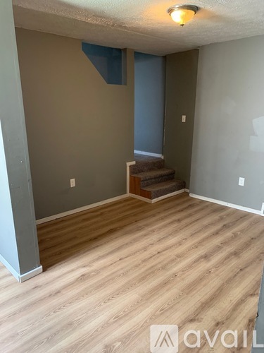 A room with wooden flooring and a staircase leading to another room.