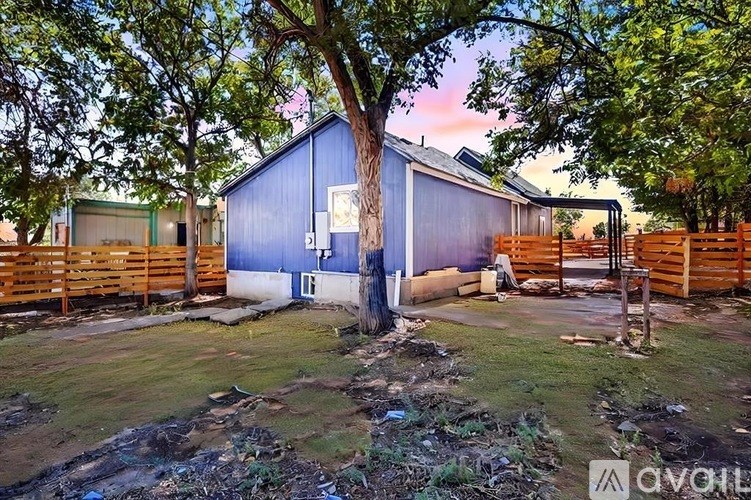 A blue building with a white door is surrounded by trees and wooden fences.