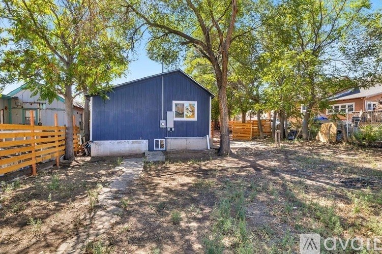 A blue building with a white door is surrounded by trees and a wooden fence.