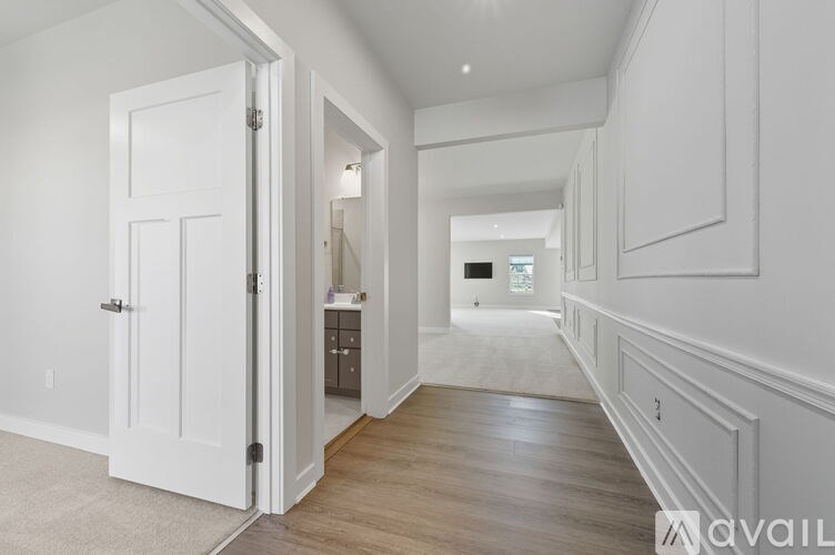 A white door is open to a hallway with wood floors and white walls.